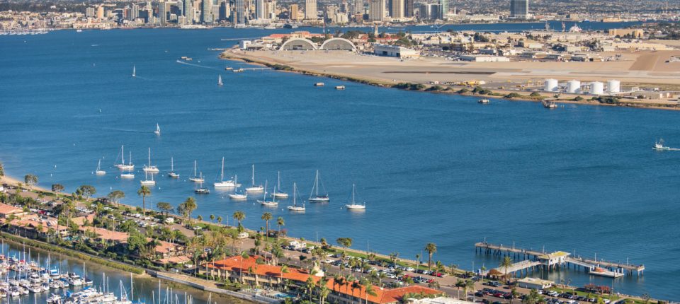 Aerial view of Shelter Island with hotels, boats in a marina, and San Diego in the distance