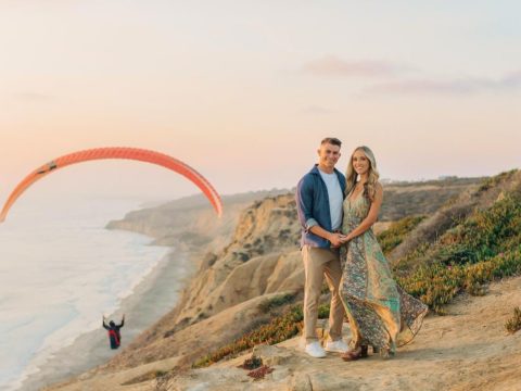 couple standing on cliff at torrey pines with hanglider in background