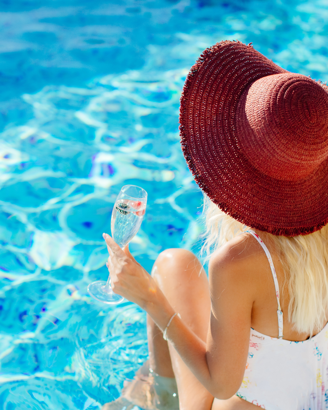 a woman sitting by the pool in a red sunhat