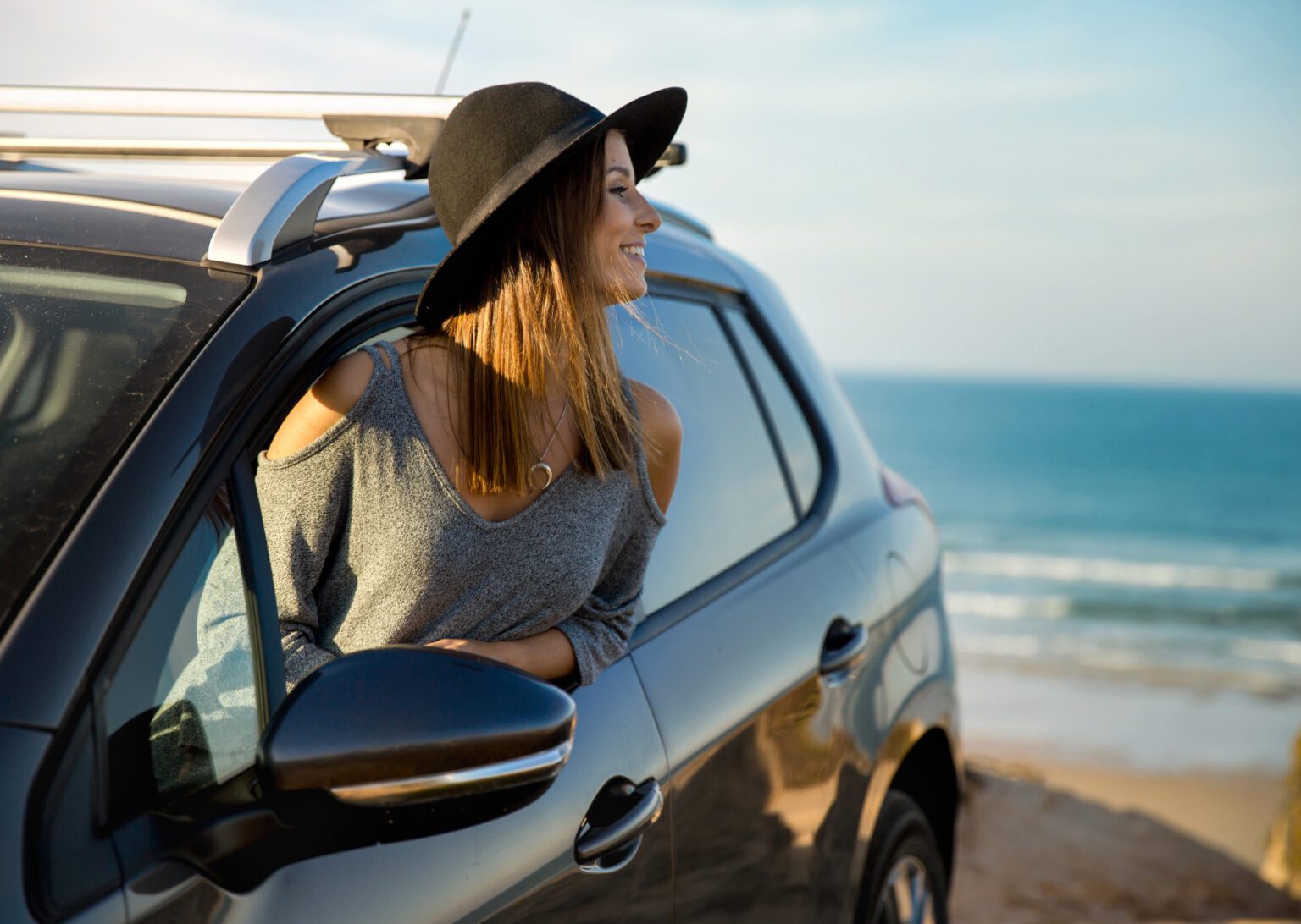 a woman hanging out the window of her car looking at the beach