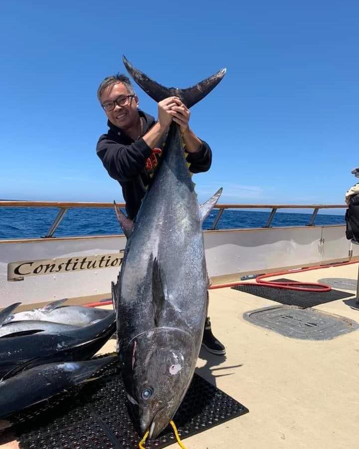 a man on a boat holding up a large tuna