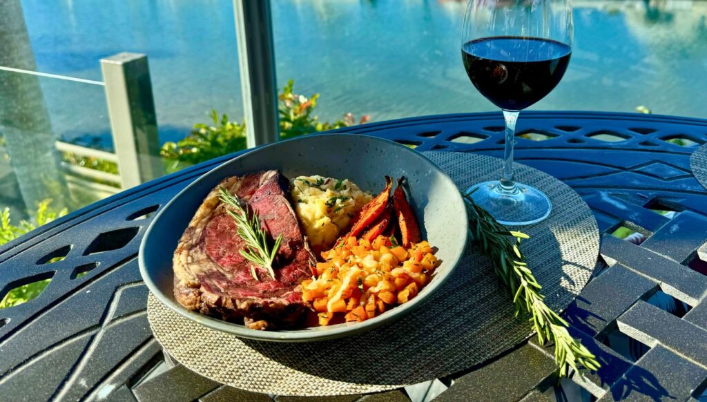 Prime rib plate on table with glass of wine in front of marina
