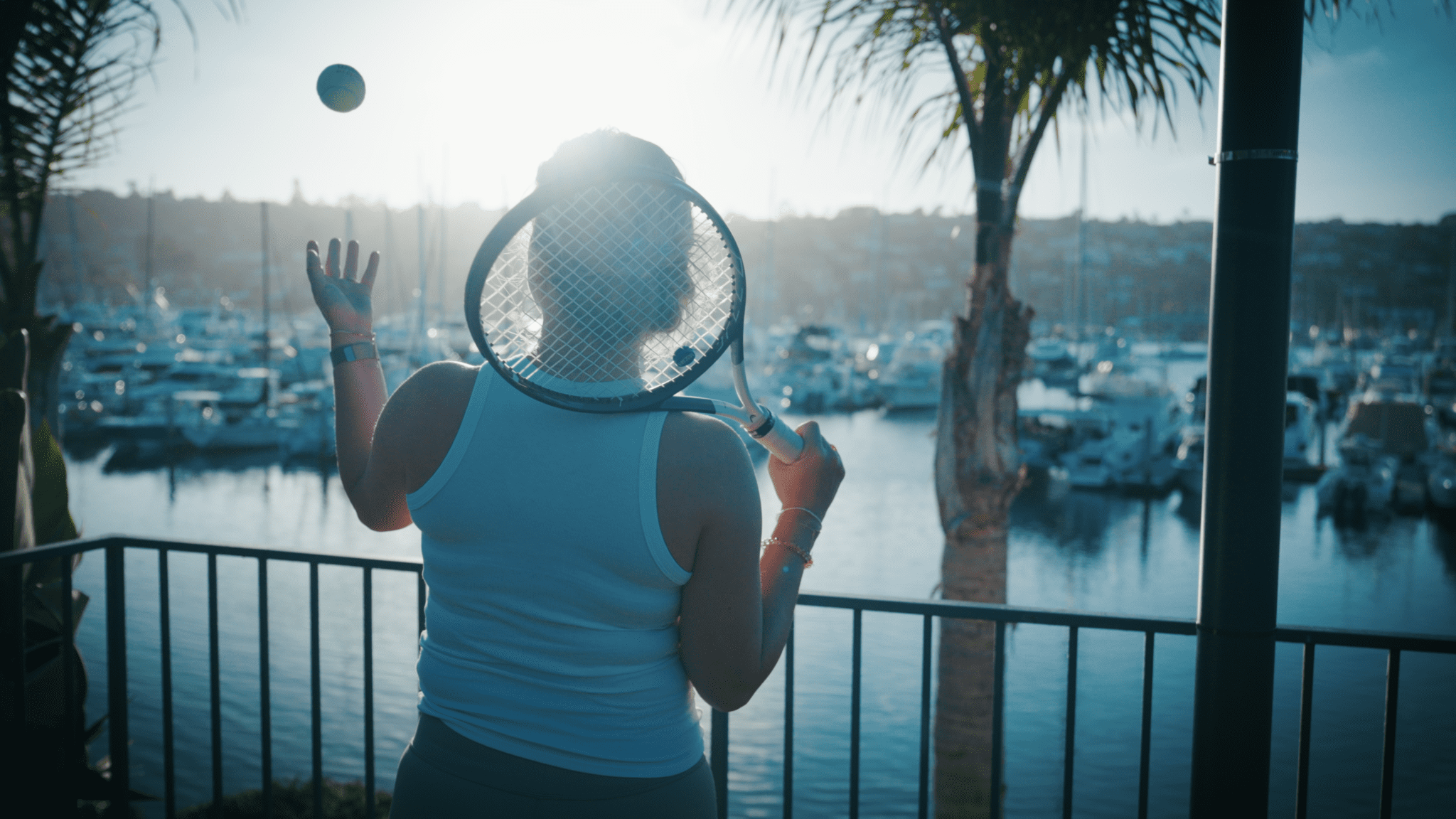 Girl holding tennis racket with ball in air along a marina